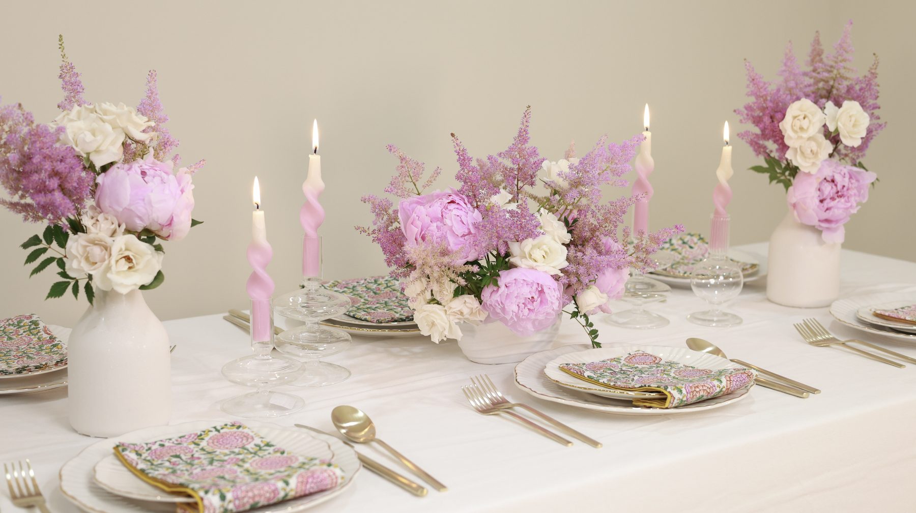 A long candlelit table styled with pink peony, astilbe, and white rose arrangements.