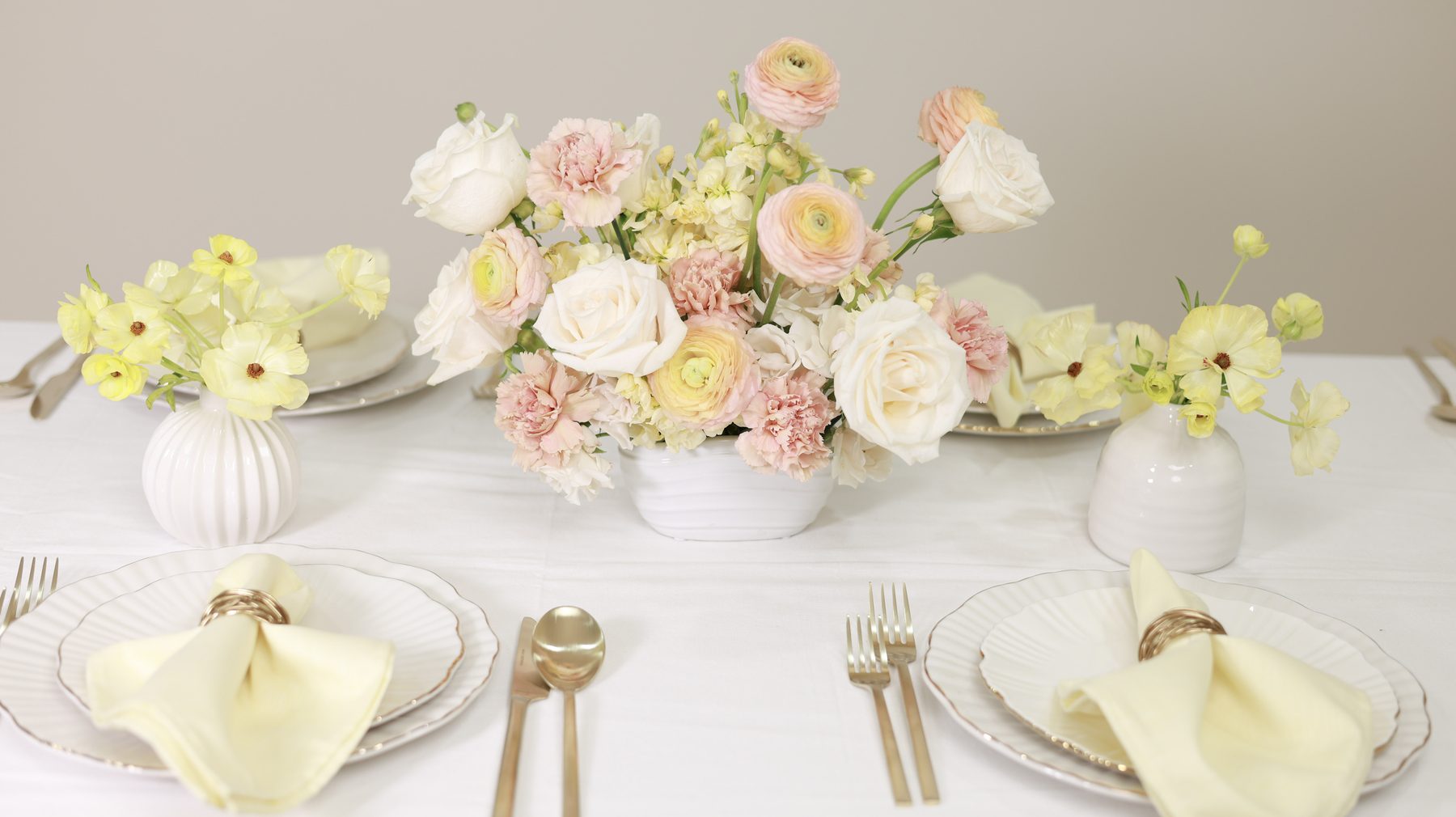 A table styled with a blush and cream floral arrangement, flanked by two smaller vases.
