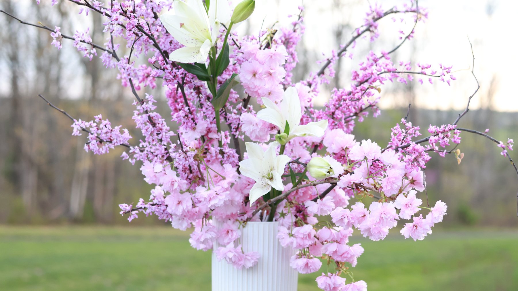 Cherry blossom and redbud branches with white lilies, outdoors.