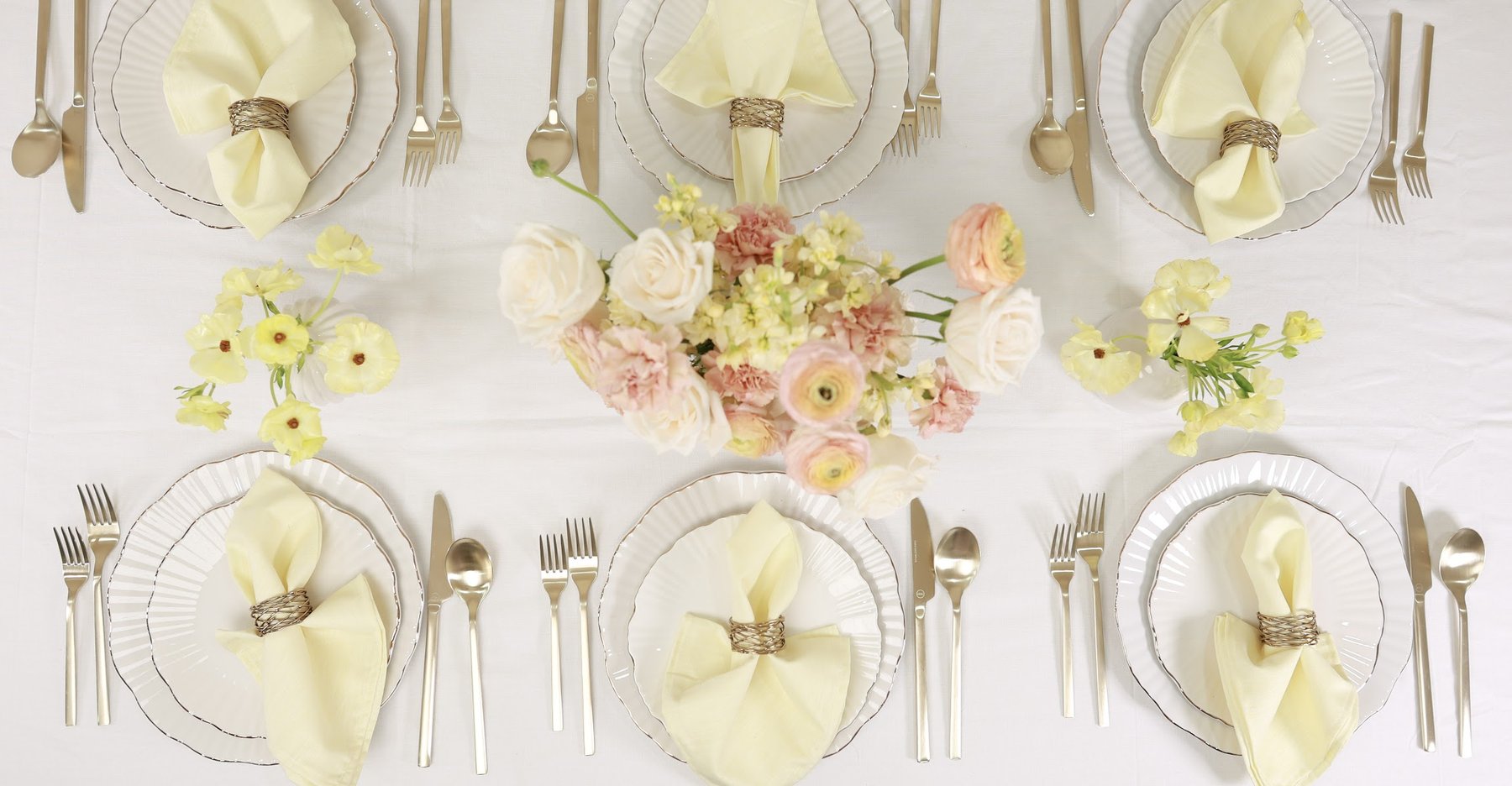 A top-down view of a butter yellow table setting with a pastel centerpiece.